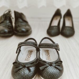 Home Close-up of shiny black children's shoes with bow design on a light wooden floor.